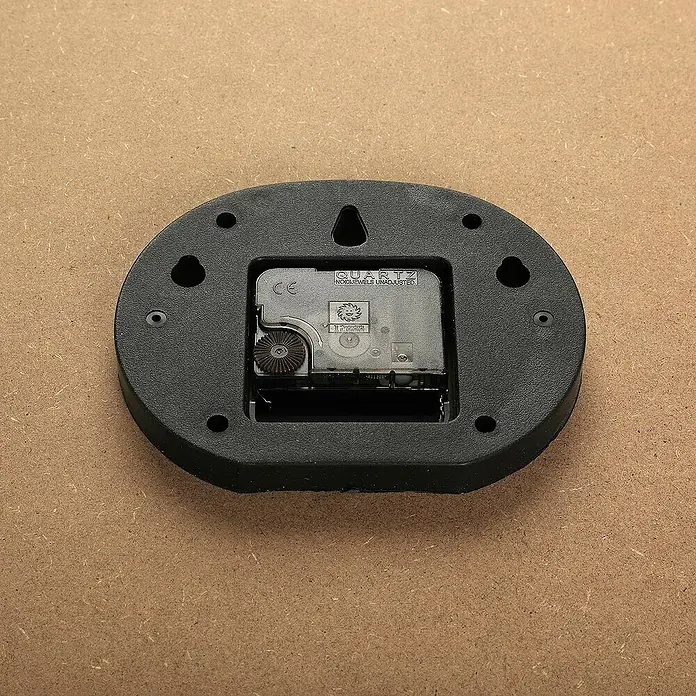 Versa Reloj de pared Madera 60 - Diámetro: 60 cm, Multicolor - Vista posterior de un mecanismo de reloj de cuarzo con colgador. Detalle del mecanismo que muestra su tecnología de cuarzo y fijación de montaje.