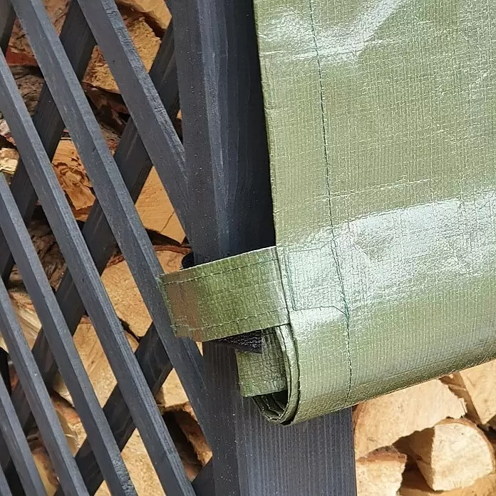 Promadino Kaminholzregal Speyer mit Wetterschutz - 120 x 68 x 148 cm, Anthrazit - Grüne gewebte Plane teilweise aufgerollt, an dunklem Holzgitter befestigt, dahinter Brennholz sichtbar.