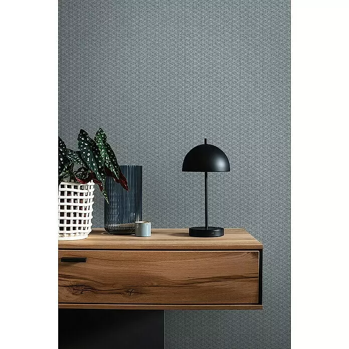 SCHÖNER WOHNEN-Kollektion Vliestapete Bouclé - Blaugrau, Uni, 10,05 x 0,53 m - Texturierte blaugraue Tapete mit dezentem Webmuster an einer Wand hinter einem stilvollen Holztisch in einem modernen Interieur.