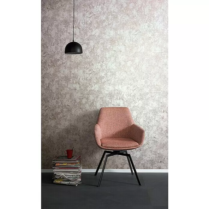 SCHÖNER WOHNEN-Kollektion Vliestapete Patina-Uni - Rosa, Betonoptik, 10,05 x 0,53 m - Korallfarbener Stoff-Sessel mit schwarzen Metallbeinen, in einem Wohnzimmer neben einem Zeitschriftenstapel und einer schwarzen Pendelleuchte darüber.