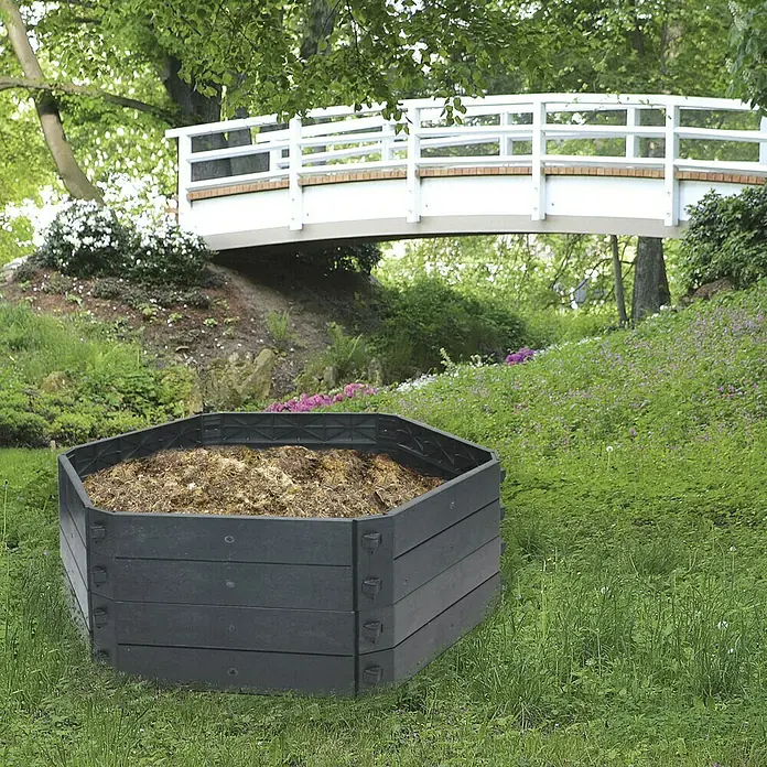 KHW Komposter SK 550 Basismodul - 550 l, Ø x H: 130 x 50 cm - Das Bild zeigt einen Kompostbehälter im Garten, der ideal für die Wiederverwertung von Gartenabfällen ist. Er fügt sich harmonisch in die Landschaft ein.