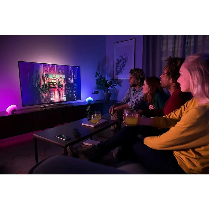 Philips Hue LED-Tischleuchte Go - 6 W, L x B x H: 15 x 15 x 7,9 cm, RGBW - Stimmungsvolles Ambiente mit der intelligenten Philips Hue Lampe, während eine Gruppe von Freunden einen Filmabend genießt.