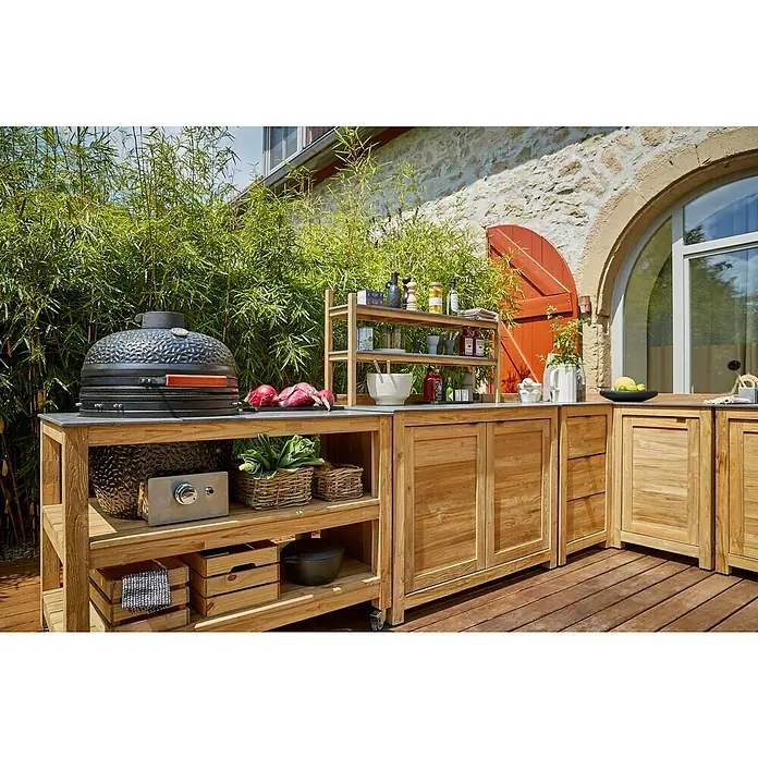 Sunfun Zoe Outdoorküchen-Modul Kamado - Braun, B x T x H: 120 x 71,5 x 89 cm, Teakholz - Eine Outdoor-Küche mit Grill, Regalen und Schränken aus hellem Holz auf einer Terrasse mit Pflanzen im Hintergrund.