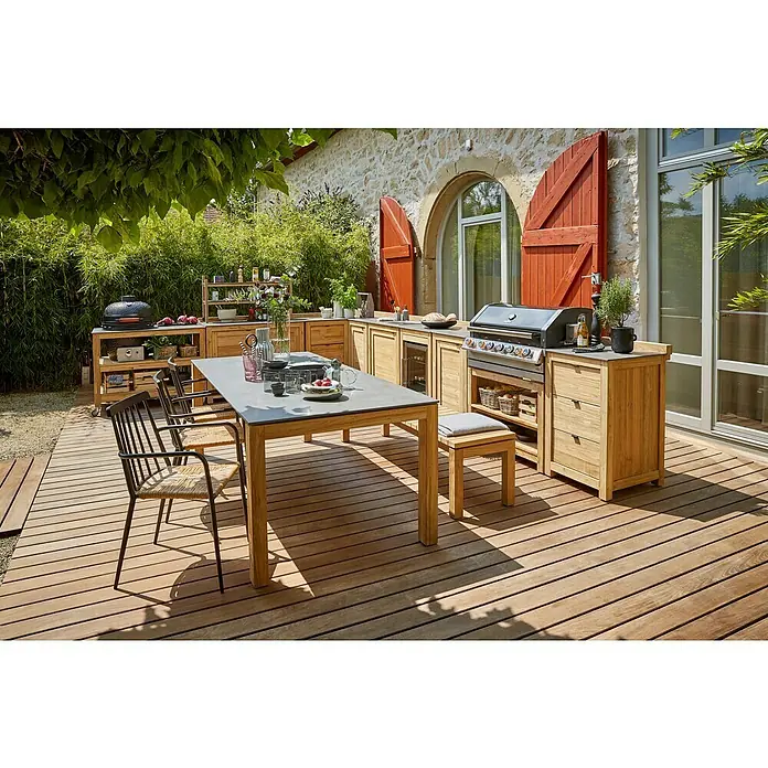 Sunfun Zoe Módulo de cocina exterior Armario con cajones - Marrón, An x Pr x Al: 58 x 63 x 92 cm, Madera de teca - Acogedora cocina exterior con parrilla, elementos de madera y mesa de comedor en una terraza bajo toldo verde.