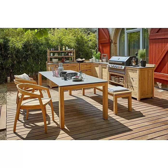 Sunfun Zoe Outdoorküchen-Modul Doppelschrank - Braun, B x T x H: 120 x 63 x 92 cm, Teakholz - Outdoor-Küche und Essbereich aus Teakholz mit grauen Arbeitsplatten, Grill und passender Essgruppe auf einer Holzterrasse.