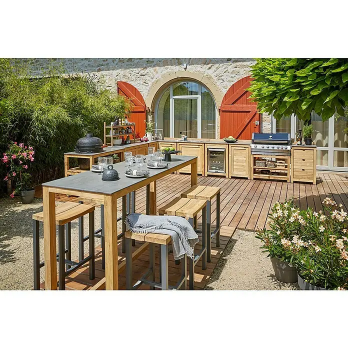 Sunfun Zoe Cocina exterior Armario bajo - Marrón, An x Pr x Al: 93 x 57,5 x 66 cm, Madera de teca - Un espacio al aire libre con muebles de teca, que incluye una mesa, taburetes, una parrilla y armarios, creando un ambiente de cocina al aire libre elegante y funcional.