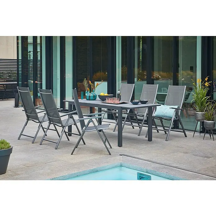 Sunfun Gartenmöbel-Set Maja/Maja Slim - 7 -tlg., Glas, Anthrazit, Tischplatte ausziehbar - Eine graue Gartentischgruppe mit sechs Stühlen steht auf einer Terrasse neben einem Pool. Die Möbel wirken modern und stilvoll.