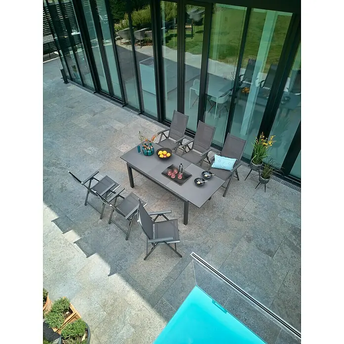 Sunfun Gartenmöbel-Set Maja/Maja Slim - 7 -tlg., Glas, Anthrazit, Tischplatte ausziehbar - Ein Gartentisch mit Stühlen auf einer Terrasse, dekoriert mit Blumen und Getränken, bietet einen stilvollen Außenbereich für Mahlzeiten und Entspannung.