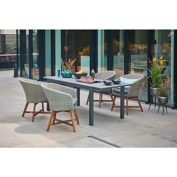 Sunfun Gartenmöbel-Set Maja/Pauline - 5 -tlg., Glas, Anthrazit/Naturbraun/Bambus Grey, Tischplatte ausziehbar - Ein grauer Gartentisch mit vier Rattanstühlen und Holzakzenten auf einer Terrasse. Die Sitzgruppe ist mit Geschirr dekoriert.