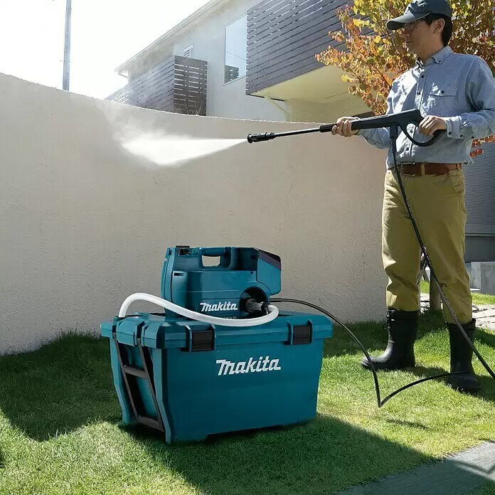 Makita LXT 18V Akku-Hochdruckreiniger DHW080ZK - 36 V, Ohne Akku, 80 bar, Fördermenge: 380 l/h - Türkisfarbener Makita Hochdruckreiniger mit passendem Wassertank, von einem Mann zum Reinigen einer Wand benutzt.