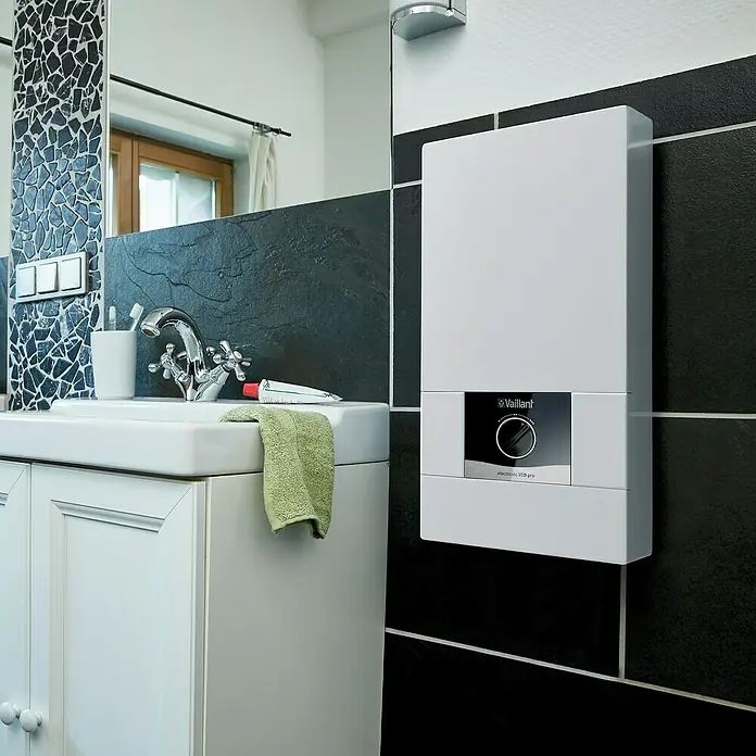 Vaillant Durchlauferhitzer VED E 24/8 B - 24 kW, Elektronisch, Geschlossen - Badezimmeransicht mit einem Vaillant ecoTEC VED pro Warmwasserbereiter an einer schwarz gefliesten Wand über einem Waschbecken.