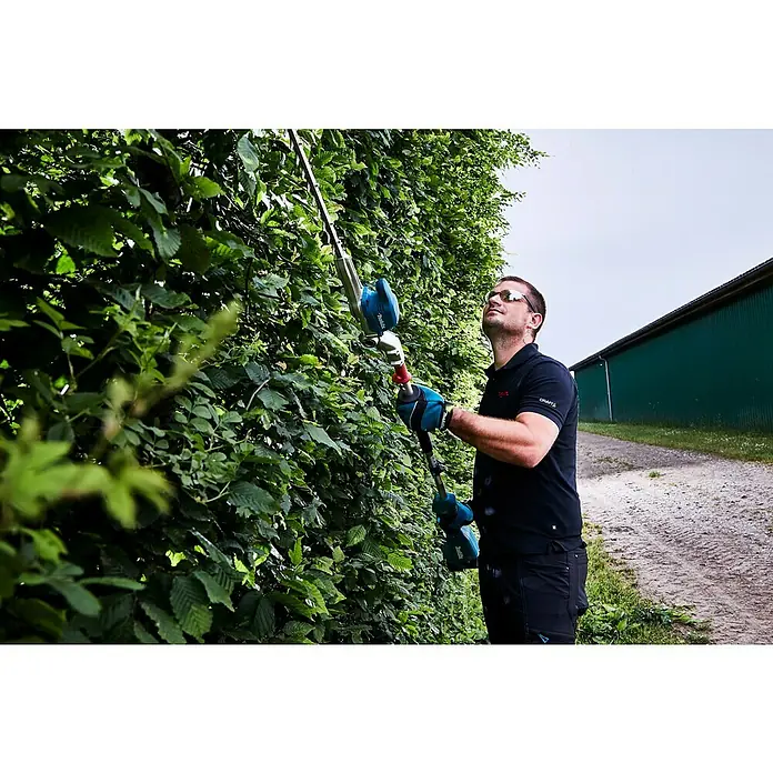 Makita LXT 18V Akku-Heckenschere DUN500WZ - 18 V, Li-Ionen, Ohne Akku - Ein Mann schneidet eine hohe Hecke mit einer Makita Akku-Heckenschere. Die Heckenschere hat einen Teleskopstiel für hohe Reichweiten.