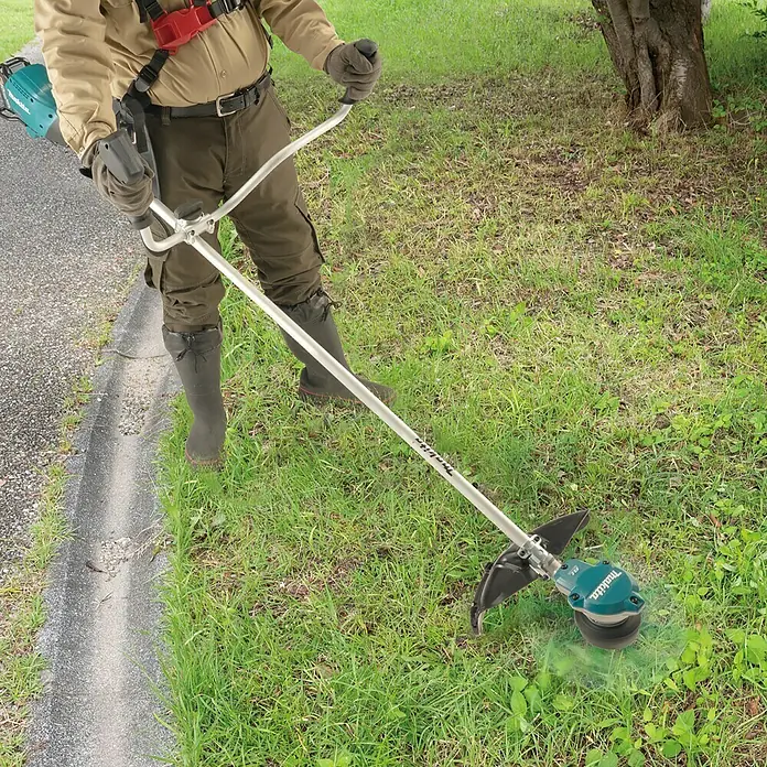 Makita XGT 40V max. Akku-Freischneider UR002GZ01 - 40 V, Ohne Akku - Eine Person trimmt Gras mit einem Makita Akku-Rasentrimmer. Das Gerät ist hellblau und silber und hat einen schwarzen Schutz.