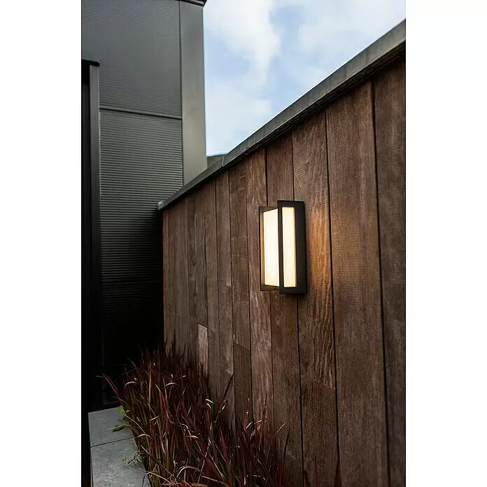 Lutec Qubo Aplique exterior LED Qubo - 17,3 W, 7,1 x 11 x 22 cm, Antracita, IP54 - Lámpara de pared exterior rectangular negra moderna, con luz cálida, montada en una valla de madera rústica.