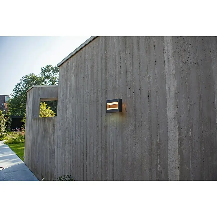 Lutec Conroy LED-Außenwandleuchte - 17,8 W, 22,5 x 15,5 x 9,7 cm, Anthrazit, IP44 - Moderne Außenwandleuchte an einer Betonmauer, die warmes Licht abstrahlt. Das Design betont die Architektur des Gebäudes und sorgt für eine angenehme Atmosphäre.