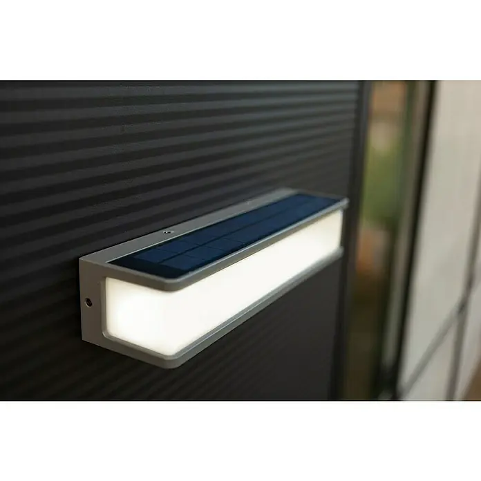 Lutec Doblo Solar-Außenwandleuchte - 16,5 W, L x B x H: 35 x 9,1 x 9 cm, Anthrazit, IP54, 1.800 lm - Nahaufnahme einer modernen, rechteckigen Solarleuchte mit silbernem Rahmen, die an einer dunklen, horizontal gestreiften Wand befestigt ist.