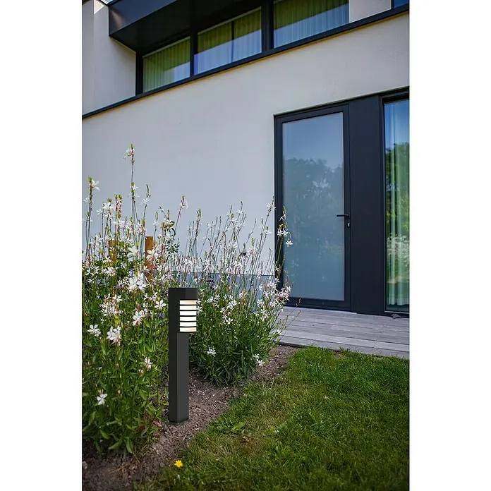 Lutec Außensockelleuchte Fulton - 40 W, Farbe Gehäuse: Schwarz matt, 17 x 16 x 75 cm, Ohne Leuchtmittel - Moderne Gartenleuchte aus dunklem Metall, eingebettet in blühende Blumen, beleuchtet stilvoll den Gartenbereich des Hauses.