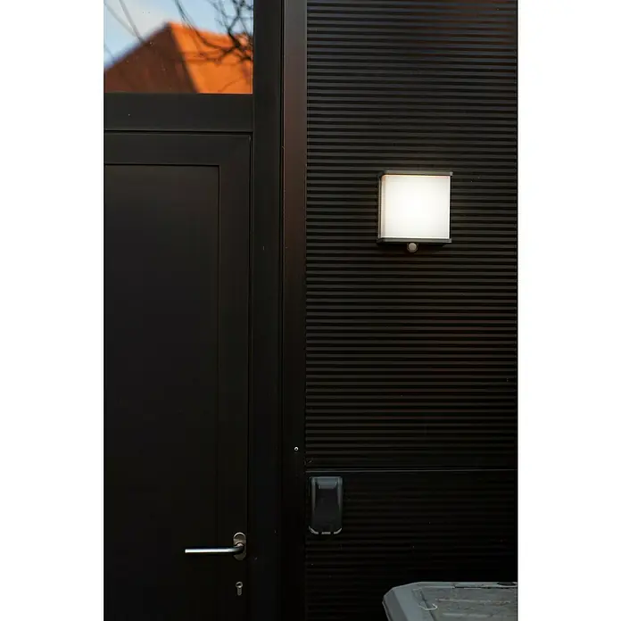 Lutec Doblo Solar-Außenwandleuchte - 12 W, L x B x H: 15 x 8,9 x 17 cm, Anthrazit, IP44, 1.000 lm - Bild einer modernen schwarzen Haustür mit einem quadratischen Wandlicht. Das Licht sorgt für eine helle, einladende Atmosphäre.