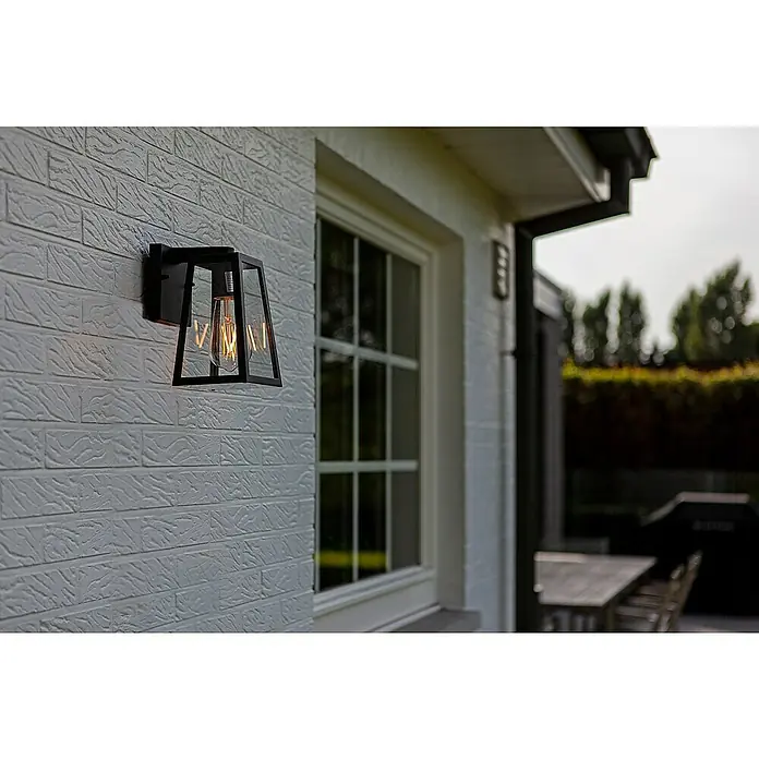 Lutec Außenwandleuchte Fia - 40 W, 16 x 14 x 21,6 cm, Schwarz matt, IP44 - Elegante schwarze Wandleuchte mit Edison-Glühbirne an einer weißen Backsteinmauer neben einem Fenster. Stilvolle Außenbeleuchtung.