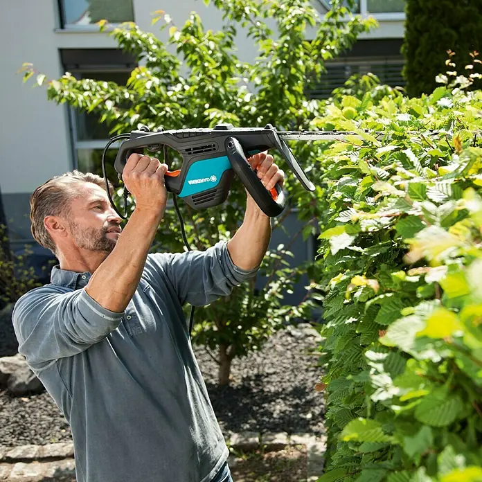 Gardena ComfortCut Elektro-Heckenschere 550/50 - 550 W, Schnittlänge: 50 cm, Max. Aststärke: 27 mm - Mann schneidet Hecke mit GARDENA Akku-Heckenschere für präzise Ergebnisse.