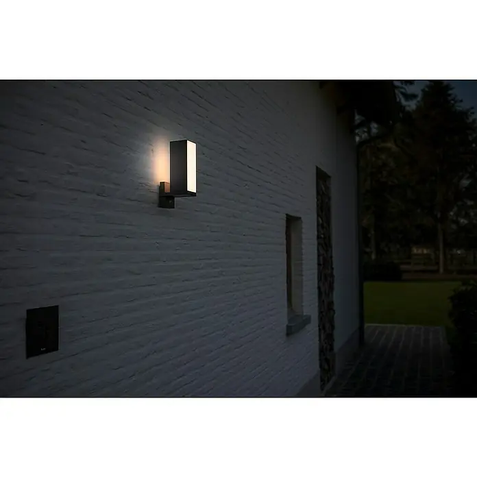 Lutec Cuba LED-Außenwandleuchte - 13 W, 14,6 x 9,3 x 30,8 cm, Anthrazit, IP54 - Moderne Außenleuchte an einer weiß gestrichenen Backsteinmauer, die warmes Licht abstrahlt. Die Lampe sorgt für eine stimmungsvolle Beleuchtung im Außenbereich.