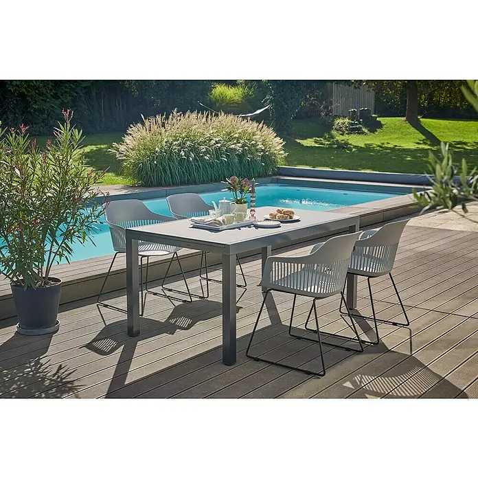 Gartensessel Annika - Black/Flint Grey, B x T x H: 57 x 60 x 82 cm - Ein grauer Gartentisch mit Stühlen steht auf einer Terrasse neben einem Pool, ideal für Mahlzeiten im Freien.