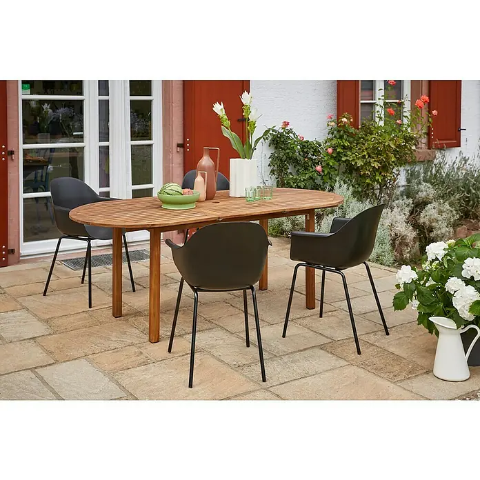 Sunfun Gartenmöbel-Set Diana/My - 5 -tlg., Holz, Naturbraun/Schwarz, Tischplatte ausziehbar - Ein Gartentisch aus Holz mit vier schwarzen Stühlen auf einer gepflasterten Terrasse, umgeben von Pflanzen und Blumen.