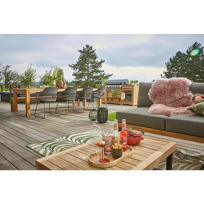 Sunfun Zoe Módulo de cocina exterior Armario con cajones - Marrón, An x Pr x Al: 58 x 63 x 92 cm, Madera de teca - Acogedora escena al aire libre con una moderna zona de descanso, una mesa de madera con bebidas y aperitivos y una parrilla al fondo.