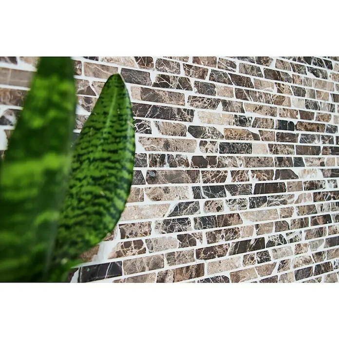 Mosaikfliese MOS BRICK 185KB - 30,5 x 30,5 cm, Braun, Matt - Nahaufnahme eines Marmor-Backsteinmosaiks mit sanften Braun-, Beige- und Grautönen, das durch ein grünes Blattwerk eines Zimmerpflanze ergänzt wird.