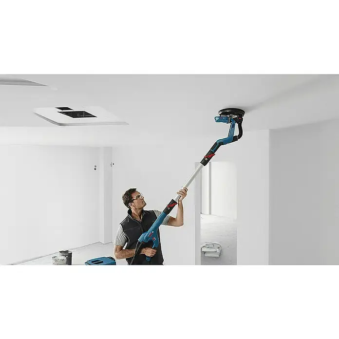 Bosch Professional Lijadora de pared y techo GTR55-225 - 550 W, Diámetro disco de lija: 225 mm - Un hombre usa una lijadora de paneles de yeso Bosch para alisar un techo en una habitación luminosa. La herramienta es el foco principal.