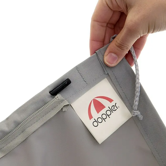 Doppler Expert Schirm-Schutzhülle - Passend für: Schirme bis Ø 350 cm - Nahaufnahme eines grauen Doppler Sonnenschirms mit Logo, an dem eine Hand eine Kordel hält. Der Schirm hat einen Reißverschluss.