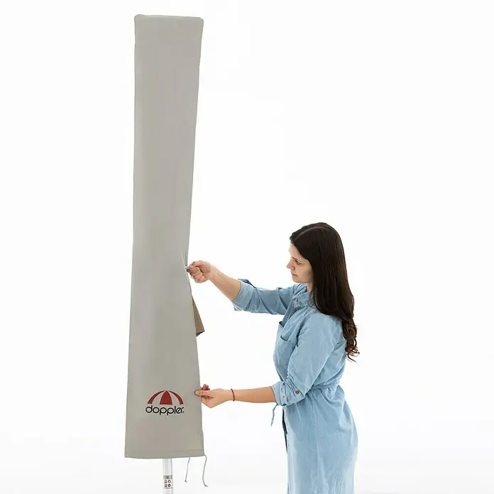 Doppler Expert Schirm-Schutzhülle - Passend für: Schirme bis Ø 350 cm - Eine Person, die eine graue Schutzhülle für einen Sonnenschirm mit dem Doppler-Logo anbringt, um diesen vor Witterungseinflüssen zu schützen.