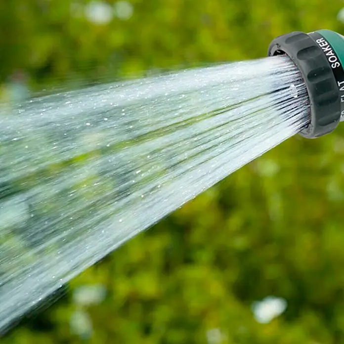 Altadex Pistola de riego rociadora 7 formas - Número de formas de rociado: 7 ud. - Primer plano de una manguera de jardín verde rociando un potente chorro de agua, ideal para el riego eficiente del jardín.
