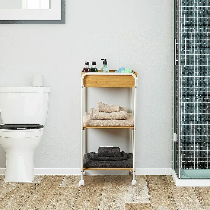 Versa Carro con ruedas 3 baldas - 40 x 29,5 x 81 cm, Metal - Imagen de un carrito de baño de tres niveles hecho de bambú y metal blanco, con toallas y artículos de aseo en los estantes, ofreciendo almacenamiento y estilo.