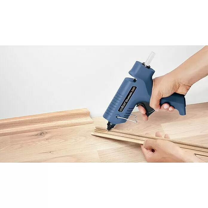 Steinel Klebepatronen Ultra Power - 40 Stk., Transparent, Durchmesser Klebepatrone: 11 mm - Hände halten eine blaue Heißklebepistole und tragen Heißkleber auf eine Holzleiste auf.