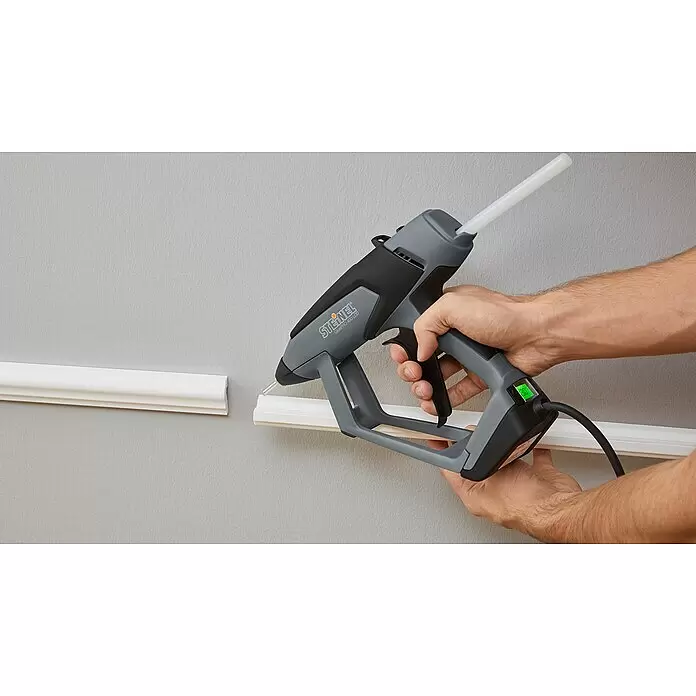 Steinel Klebepatronen Low-Melt - 20 Stk., Transparent, Durchmesser Klebepatrone: 11 mm - Graue und schwarze STEINEL GLUEPRO 400 LCD Heißklebepistole wird verwendet, um weiße Zierleisten an eine Wand zu kleben.