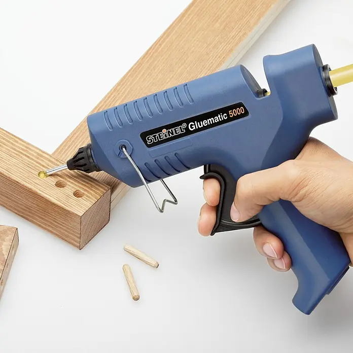 Steinel Heißklebepistole Gluematic 5000 - Durchmesser Klebepatrone: 11 mm, 500 W - Eine blaue Steinel Gluematic 5000 Klebepistole wird verwendet, um Holzstücke zu verkleben, während Holzdübel daneben liegen.