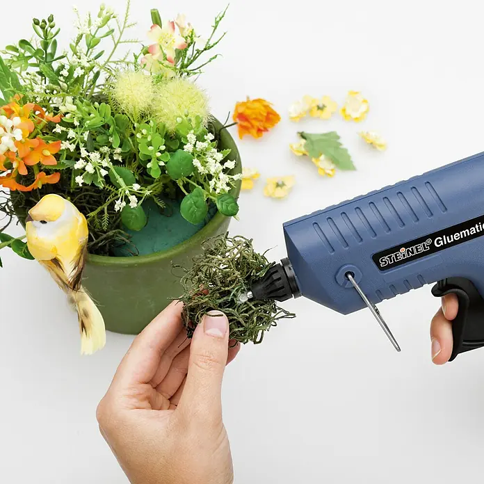 Steinel Heißklebepistole Gluematic 5000 - Durchmesser Klebepatrone: 11 mm, 500 W - Eine Heißklebepistole Steinel Gluematic wird verwendet, um Dekorationen an einem Blumenarrangement anzubringen.