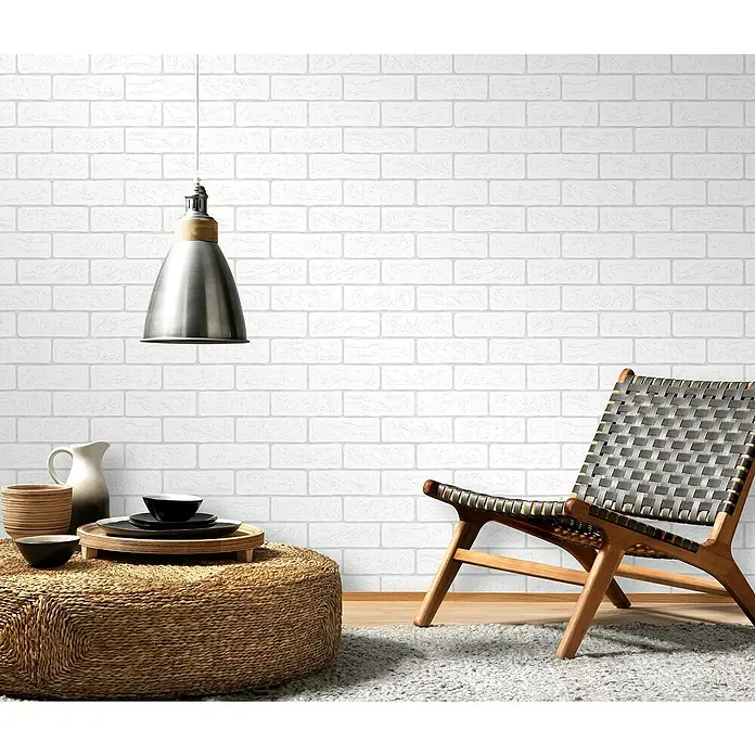 Papel pintado Ladrillo Relieve - Blanco, 10 x 0,53 m - Espacio habitable con una silla de telar de moda, una lámpara decorativa y una mesa auxiliar rústica, todo sobre un fondo de pared de ladrillo blanco.