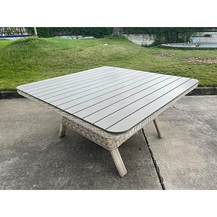 Sunfun Conjunto de muebles Milwaukee - 8 pzs., Ratán sintético, Arena - Primer plano de una mesa de patio cuadrada con tablero de listones grises y base de mimbre, en un patio exterior.