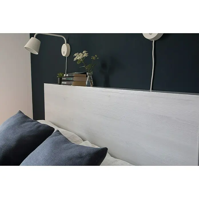 D-c-fix Holzoptikfolie - 200 x 67,5 cm, Nordic Elm, Selbstklebend, Holzstruktur - Nahaufnahme eines Bettes mit einem weißen Holzkopfende, blauen Kissen und Wandleuchten an einer dunklen Wand.