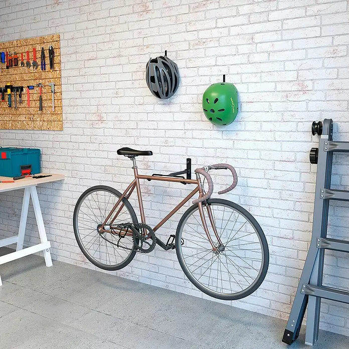 Rei Soporte de pared de bicicletas - L x An x Al: 9 x 32 x 45 cm, Acero, Montaje en la pared - Portabicicletas de pared que muestra una elegante bicicleta de carreras marrón, complementada con cascos y herramientas en la pared.