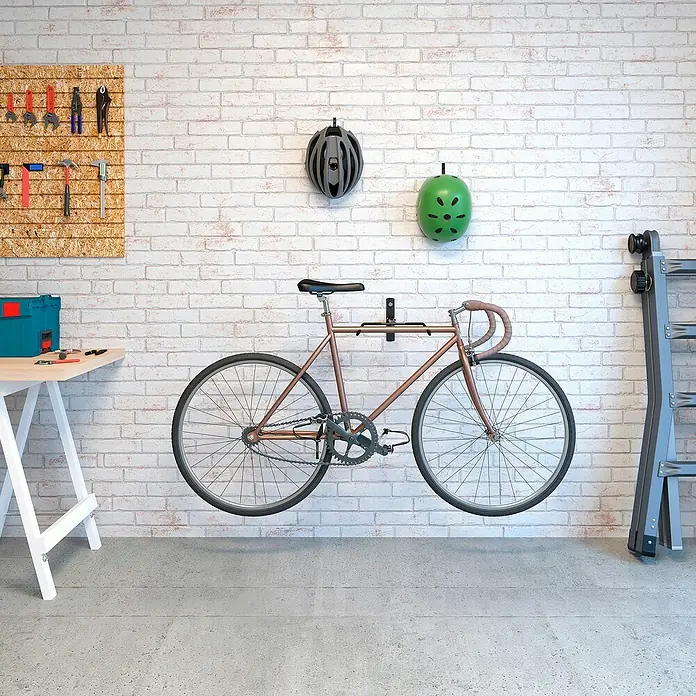 Rei Soporte de pared de bicicletas - L x An x Al: 9 x 32 x 45 cm, Acero, Montaje en la pared - Un portabicicletas de pared en un garaje, con cascos y herramientas exhibidas.