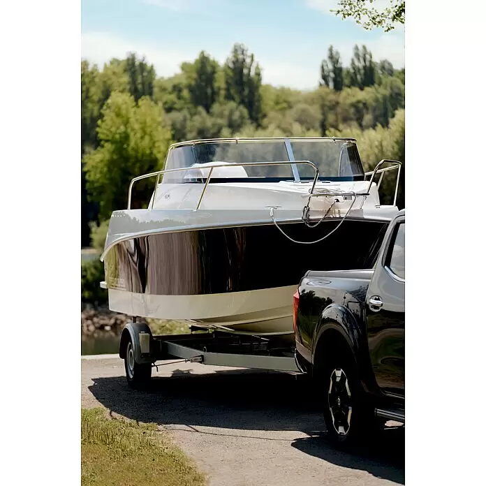 PEGAZUS GFK-Boot 550 Comfort - Umfangreiche Zusatzausstattung, Geeignet für: Max. 6 Personen, Nutzlast: 670 kg, CE-Klasse C - Weißes und dunkles Boot auf Trailer, an schwarzen Pickup angehängt, an Bootsrampe bei Bäumen.