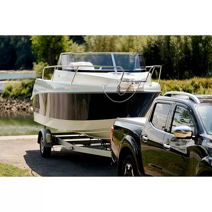 PEGAZUS GFK-Boot 550 Comfort - Umfangreiche Zusatzausstattung, Geeignet für: Max. 6 Personen, Nutzlast: 670 kg, CE-Klasse C - Ein weiß-dunkles Boot auf einem Anhänger, gezogen von einem schwarzen Pickup-Truck in Wassernähe.