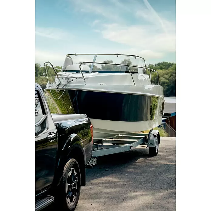 PEGAZUS GFK-Boot 550 Comfort - Umfangreiche Zusatzausstattung, Geeignet für: Max. 6 Personen, Nutzlast: 670 kg, CE-Klasse C - Schwarzer Pickup-Truck zieht ein weiß-dunkelblaues Boot auf einem silbernen Anhänger zum Wasser.