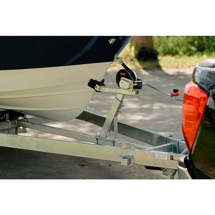 PEGAZUS GFK-Boot 550 Comfort - Umfangreiche Zusatzausstattung, Geeignet für: Max. 6 Personen, Nutzlast: 670 kg, CE-Klasse C - Nahaufnahme eines Bootstrailers mit einer AL-KO Winde, die an einem dunklen Auto befestigt ist, ideal für den sicheren Transport von Booten.