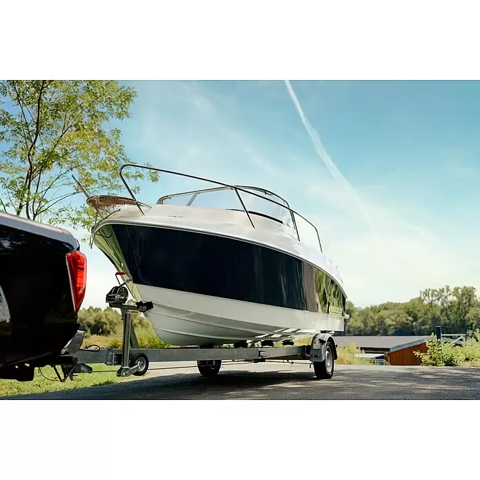 PEGAZUS GFK-Boot 550 Comfort - Umfangreiche Zusatzausstattung, Geeignet für: Max. 6 Personen, Nutzlast: 670 kg, CE-Klasse C - Ein weiß-dunkelblaues Boot auf einem grauen Anhänger, an einen schwarzen Pickup angeschlossen, bereit zum Transport.