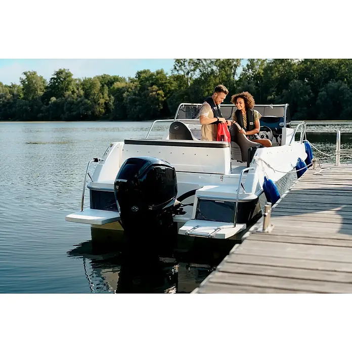 PEGAZUS GFK-Boot 550 Comfort - Umfangreiche Zusatzausstattung, Geeignet für: Max. 6 Personen, Nutzlast: 670 kg, CE-Klasse C - Ein Paar auf einem weißen Motorboot am Dock, das eine schwarze Motor aufweist, mit Bäumen und Wasser im Hintergrund.