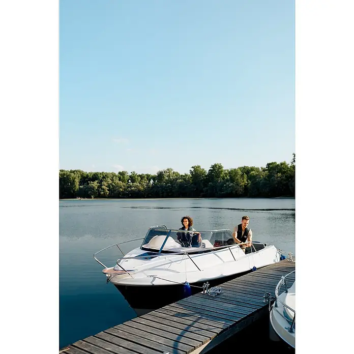 PEGAZUS GFK-Boot 550 Ready to Go 100 - Motorleistung: 73,6 kW, Geeignet für: Max. 6 Personen, Norm: CE-Klasse C - Ein strahlend weißes Motorboot liegt an einem Holzsteg vor ruhigem Wasser und üppigem Grün. Zwei Personen genießen die Fahrt.